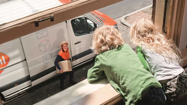 Pakketbezorger met kinderen hangend uit het raamkozijn