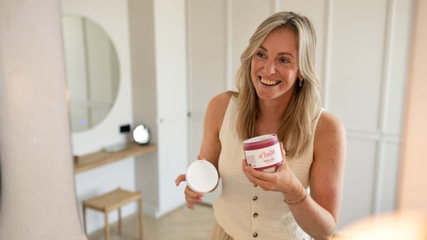 Vrouw opent een verzorgingsproduct terwijl ze lachend in de spiegel kijkt