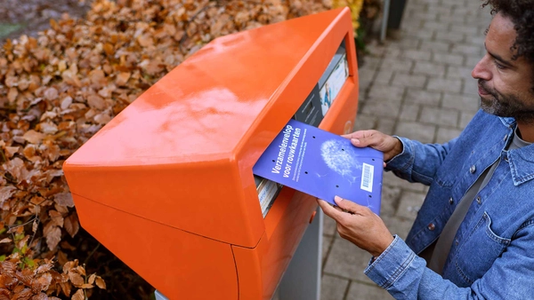 Man doet een envelop met rouwkaarten in de oranje brievenbus