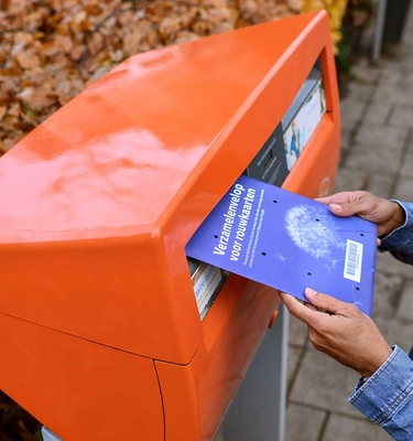 Man doet een envelop met rouwkaarten in de oranje brievenbus