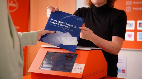 Man doet een envelop met rouwkaarten in de oranje brievenbus