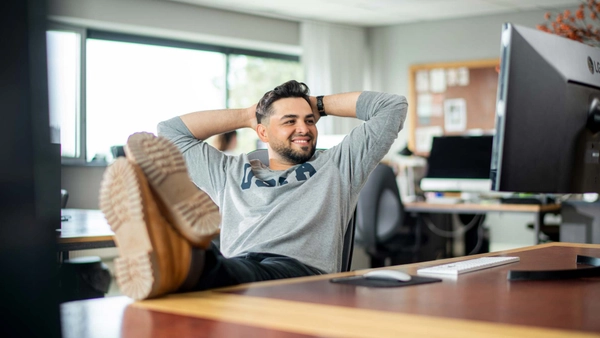 Webshopondernemer kijkt tevreden naar een computerscherm en leunt achterover in een bureaustoel met voeten op het bureau