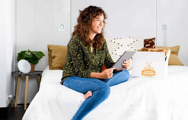 Lachende vrouw op bed met een pakket 'Groetjes uit Holland' en een tablet in haar hand