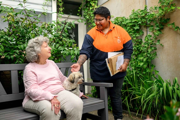 Postbezorger maakt een praatje met een oudere dame op een bankje. 