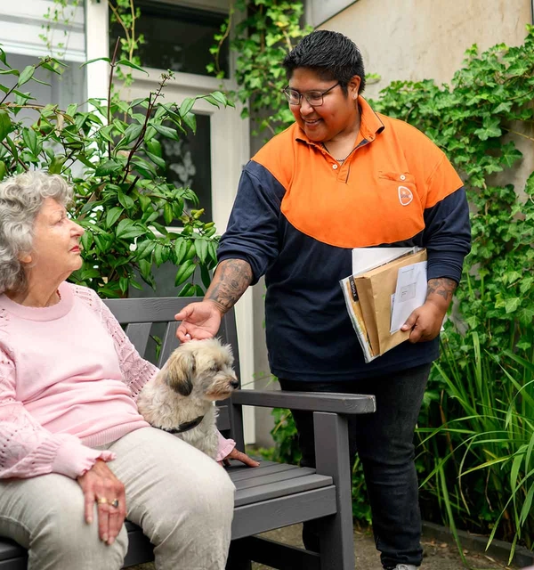 Postbezorger maakt een praatje met een oudere dame op een bankje.