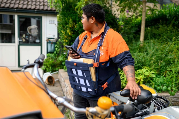 Postbezorger kijkt bezorgd naar een huis tijdens de postronde.
