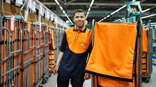 Medewerker in PostNL-kleding naast een rolcontainer in een sorteercentum