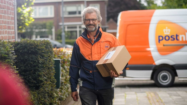 Vrolijke pakketbezorger loopt met pakket onder de arm over straat