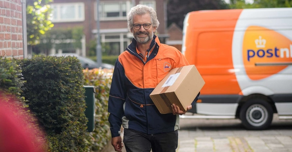 Vrolijke pakketbezorger loopt met pakket onder de arm over straat