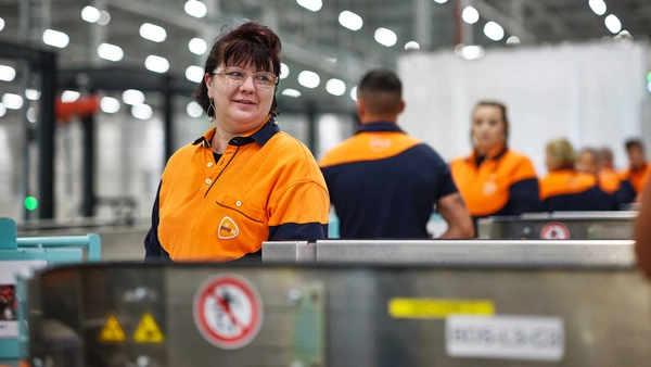 Meerdere PostNL-medewerkers aan een lopende band in een sorteercentrum