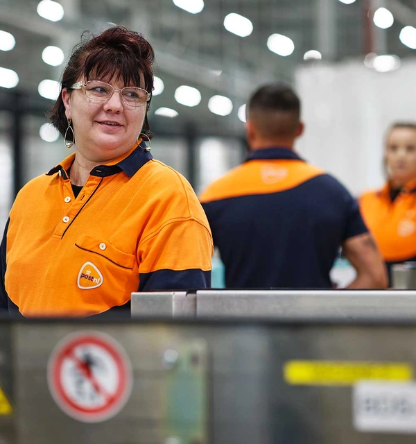 Meerdere PostNL-medewerkers aan een lopende band in een sorteercentrum