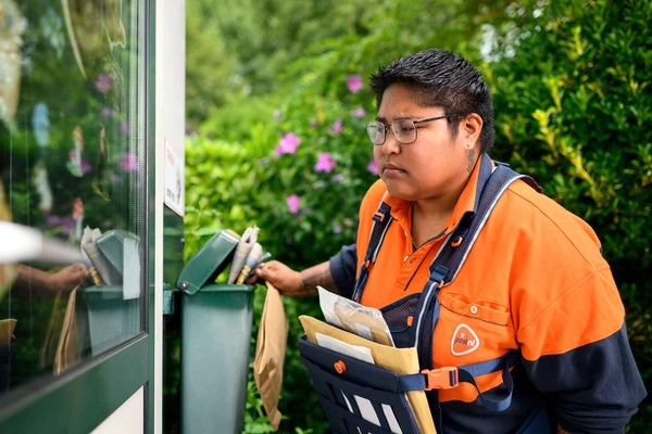 Postbezorger kijkt bezorgd door een raam tijdens het bezorgen van de post. 