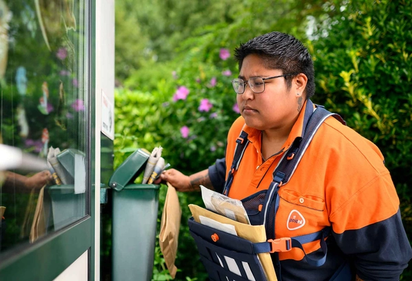 Postbezorger kijkt bezorgd door een raam tijdens het bezorgen van de post.