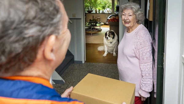 Pakketbezorger geeft een pakket aan een vrouw met een hond op de achtergrond