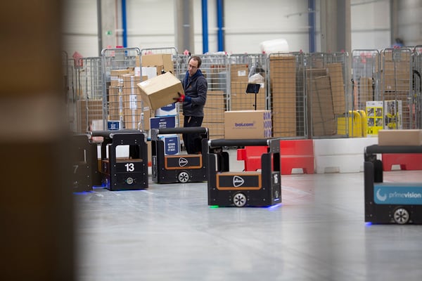 Medewerker tilt een doos terwijl autonome sorteerrobots rijden in een sorteercentrum.