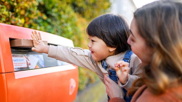 Kindje stopt een brievenbuspakketje in een brievenbus