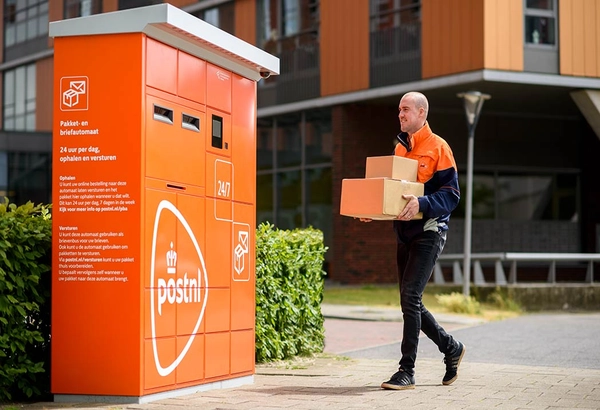 Pakketbezorger loopt met een stapel pakketjes naar een pakketautomaat