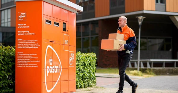 Pakketbezorger loopt met een stapel pakketjes naar een pakketautomaat