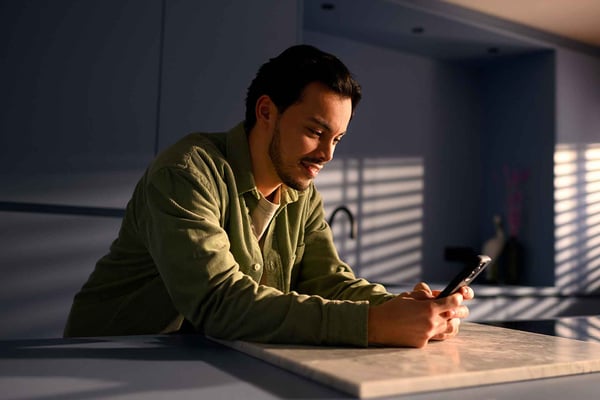 Man gebruikt een smartphone aan een keukentafel in huiselijke setting.