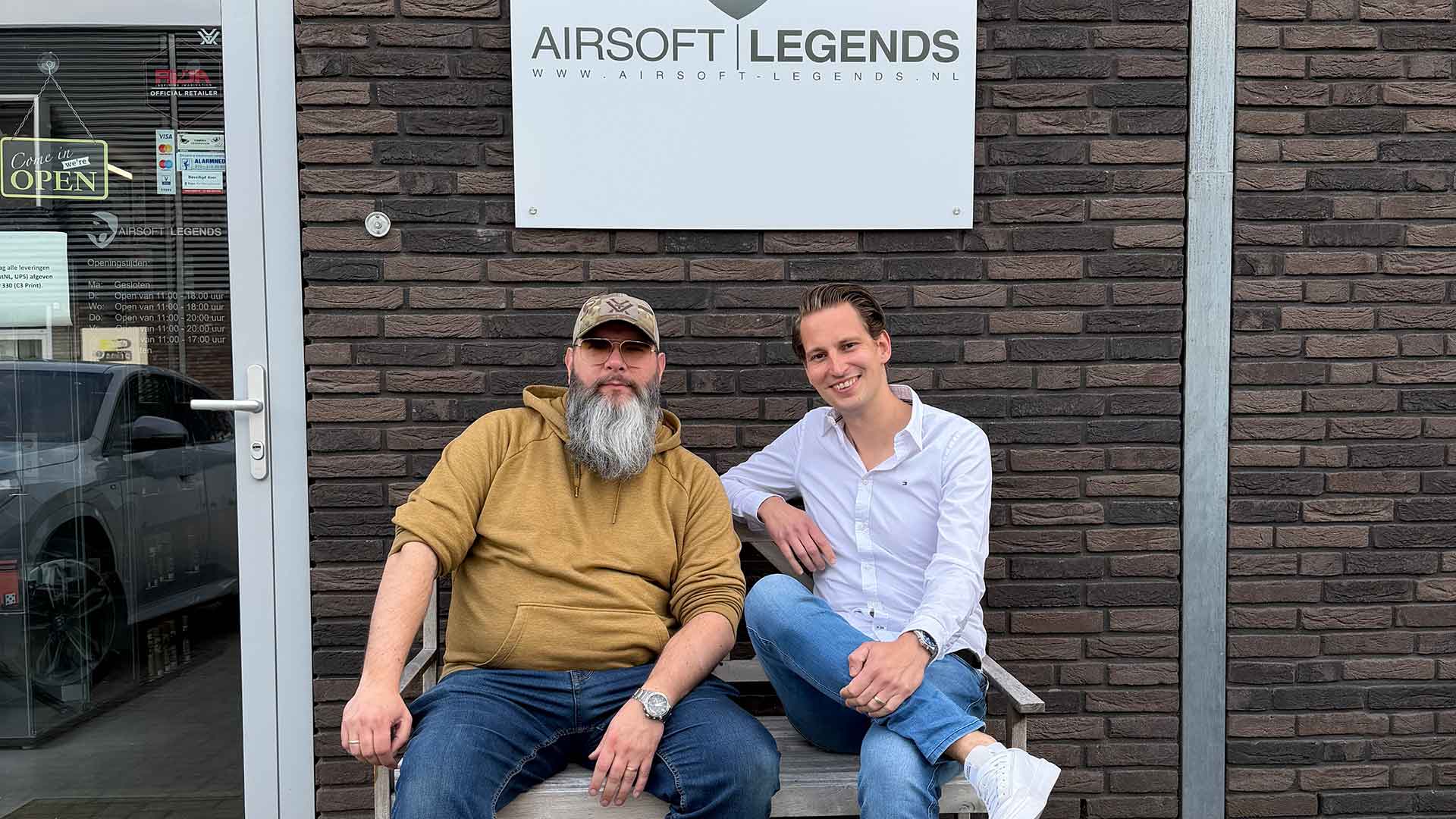 Twee mannen zitten op een bank voor het pand van Airsoft Legends