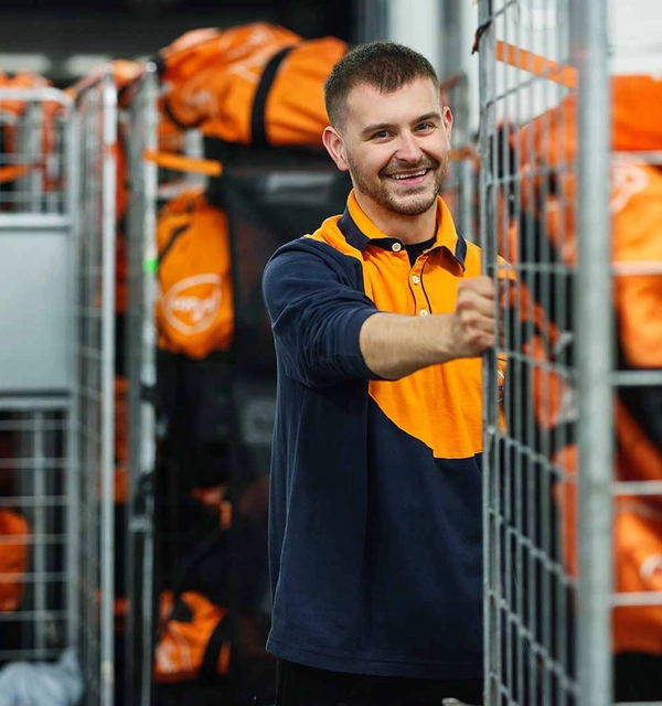 Medewerker in PostNL-kleding rolt een rolcontainer weg in een sorteercentrum