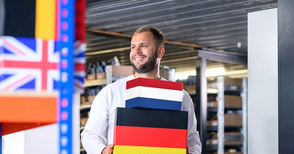 Magazijnmedewerker draagt pakketten in de kleuren van de Nederlandse en Duitse vlag