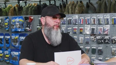 Een man houdt een kaartje vast aan een tafel in een winkel met airsoft- en outdoorartikelen