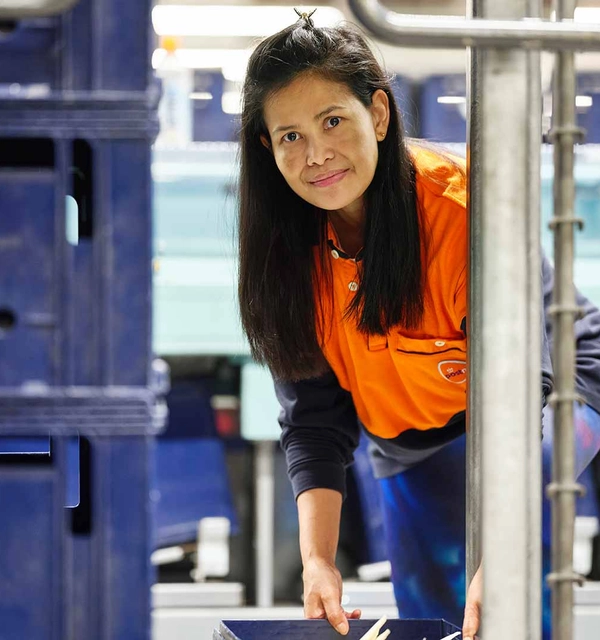 Vrouw in PostNL-kleding tilt een bak met post uit een rolcontainer op een sorteercentrum