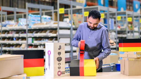 Webshopmedewerker in een magazijn plakt een pakket dicht met daarop de Duitse vlag