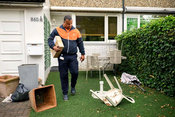 Pakketbezorger loopt door een tuin vol rommel.