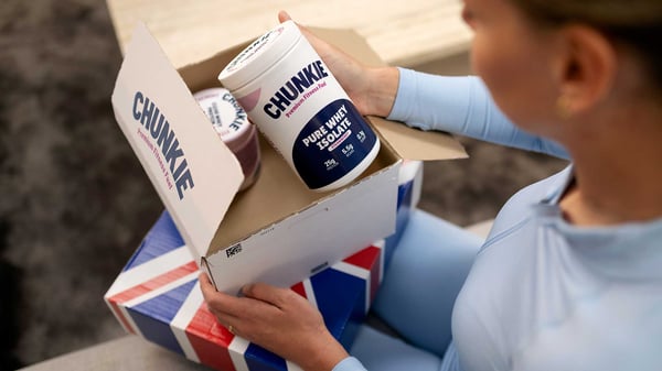 Vrouw opent thuis op de bank een pakket met fitness-supplementen