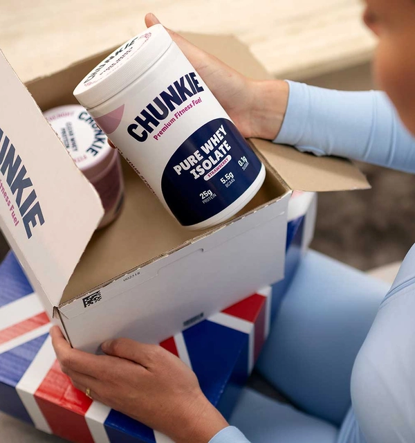 Vrouw opent thuis op de bank een pakket met fitness-supplementen